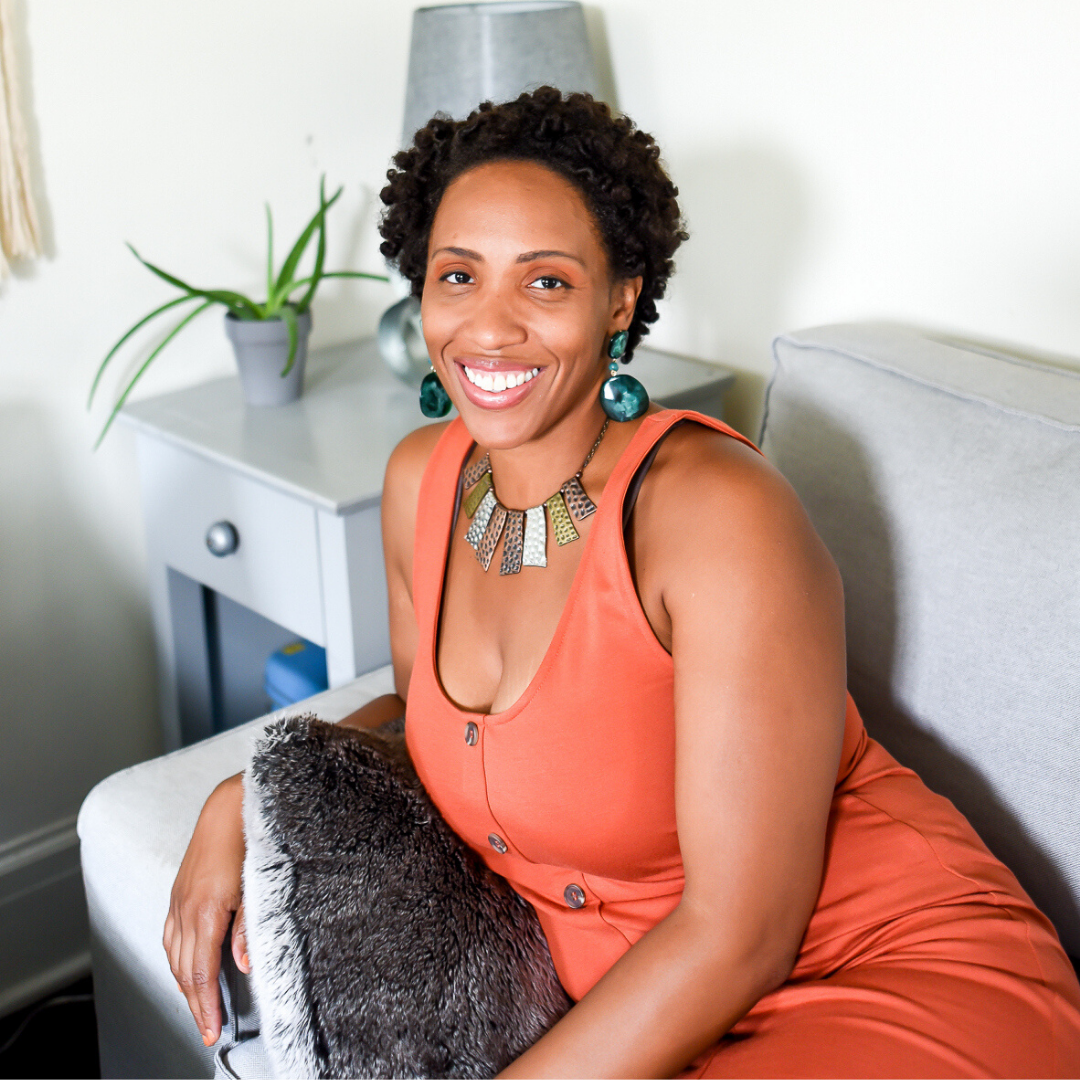 Muffy Mendoza sitting on a couch wearing an orange dress, smiling