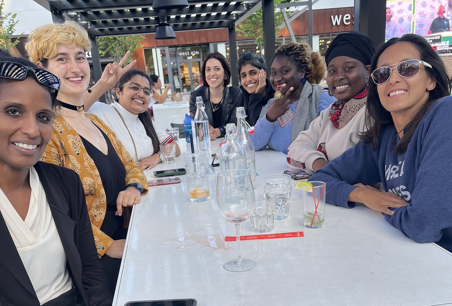 Members of CONVERGE and EMBRACE sitting at a table outside with various drinks and food sitting on the table.